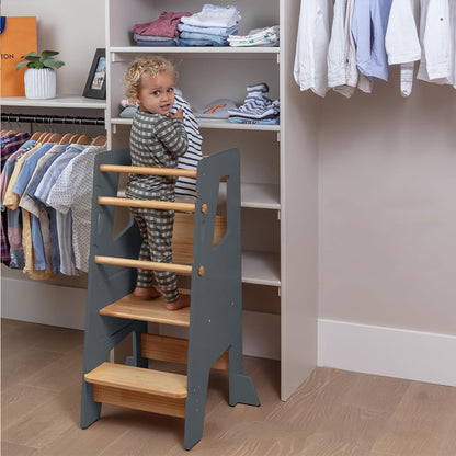 Faltbarer Montessori-Lernturm aus naturbelassenem und grauem Holz mit gelbem Blumendetail – ideal für Kleinkinder bei Aufgaben in Küche und Bad