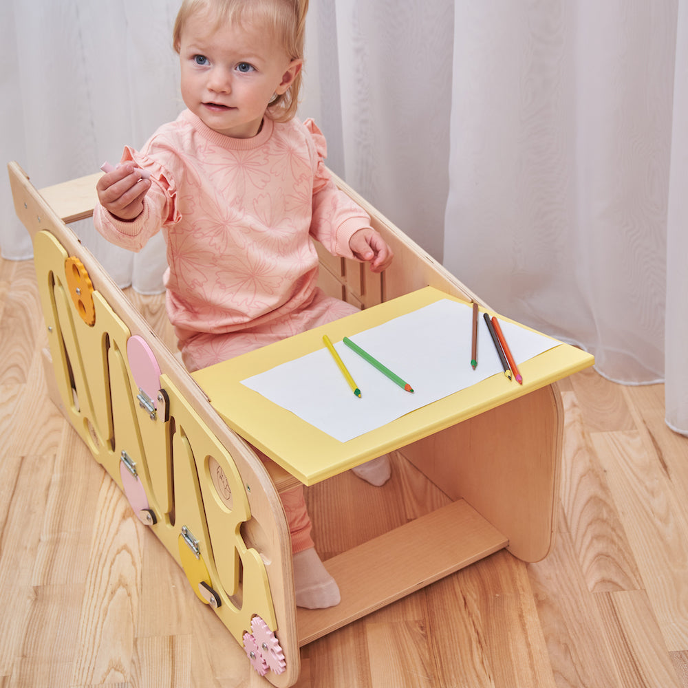Montessori Lernturm aus Naturholz mit gelbem seitlichem Busy Board, ausgestattet mit interaktiven Zahnrädern, Schiebereglern und verschließbaren Elementen für Kleinkinder.
