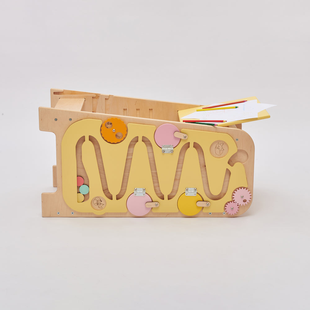 Montessori Lernturm aus Naturholz mit gelbem seitlichem Busy Board, ausgestattet mit interaktiven Zahnrädern, Schiebereglern und verschließbaren Elementen für Kleinkinder.